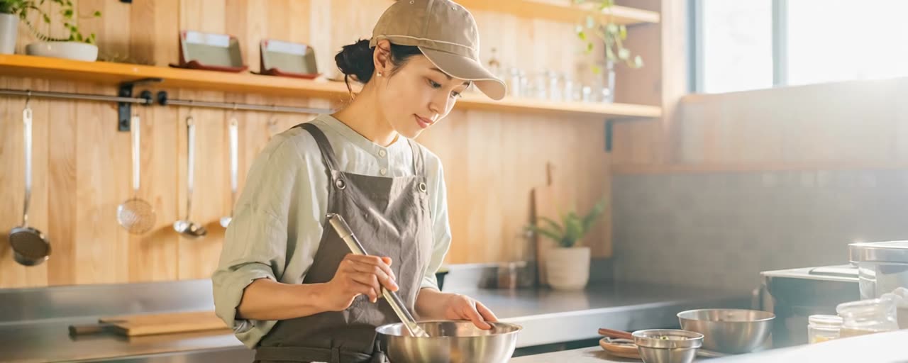飲食店の厨房で、エプロン姿の店主が調理台で仕込みをしている様子